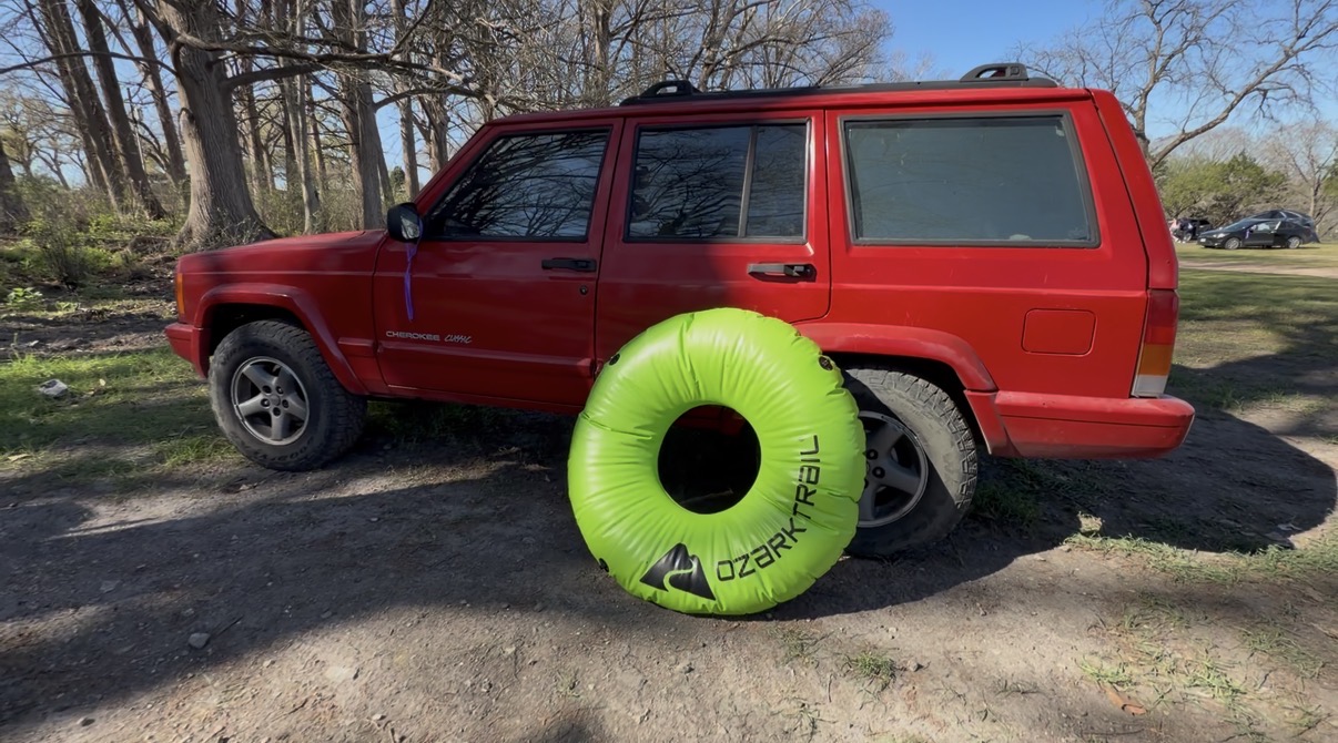 This is a photo of my boyfriend's 1999 jeep. He calls it red 40 because of how bright red it is. There is a green river tube posed next to it.